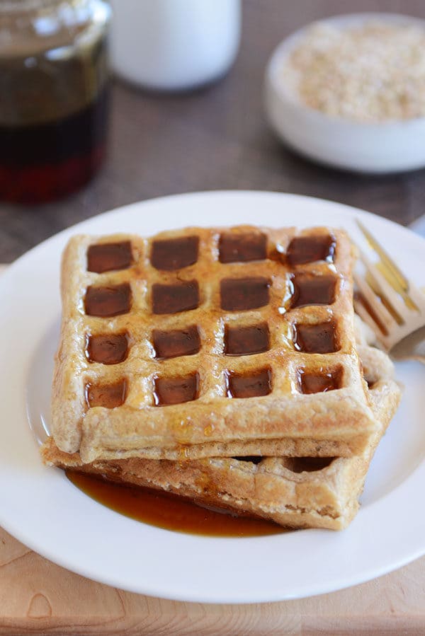 Two thick waffles covered in syrup on a white plate. 