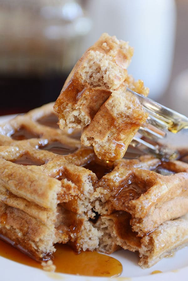 A fork taking a bite out of two stacked syrupy waffles. 