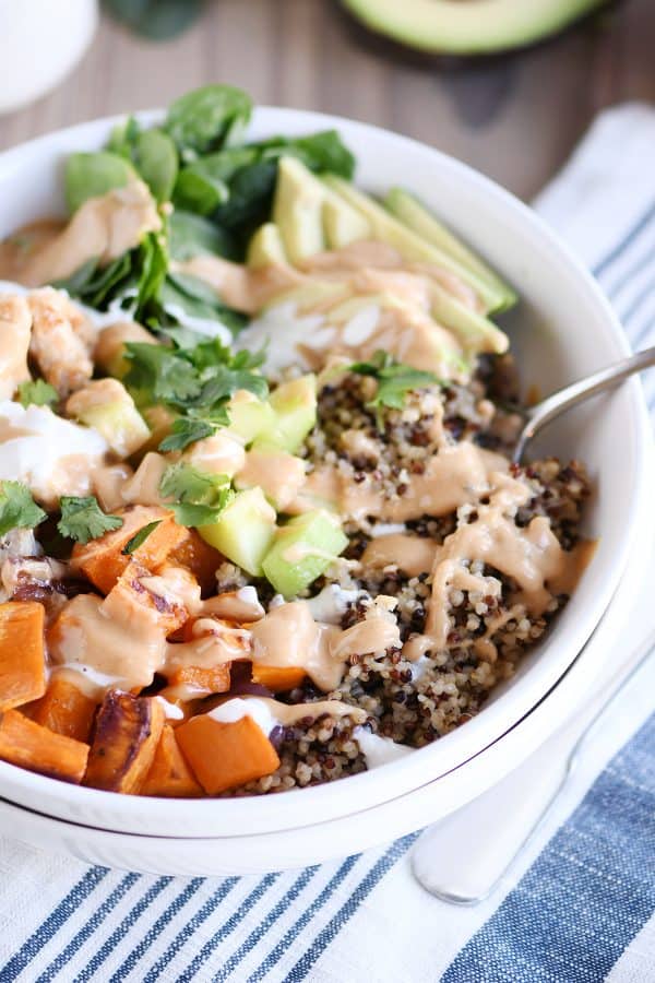 Assembled Buddha bowl recipe with peanut sauce in white bowl with fork.