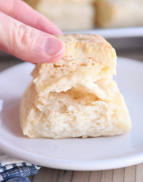 Pulling apart super flaky buttermilk biscuit on white plate.
