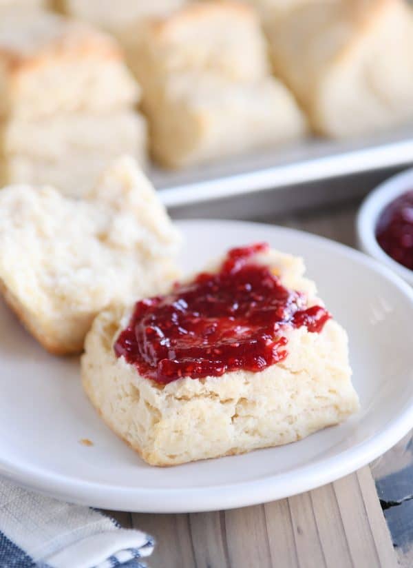 Super flaky buttermilk biscuit on white plate cut in half with jam and butter.