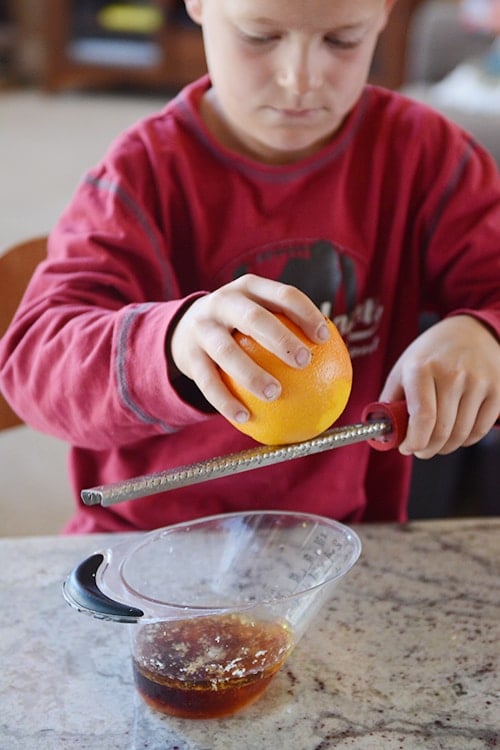 A little boy grating an orange over a microplane. 