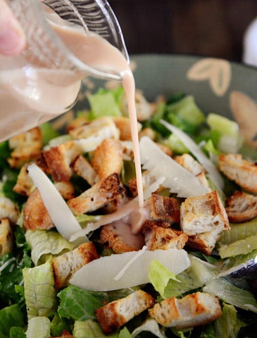 Dressing getting poured over a large bowl of ceasar salad. 