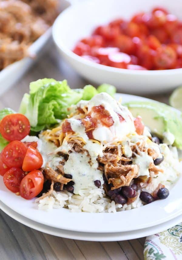 White plate with cilantro lime rice, black beans, sweet pork and toppings.