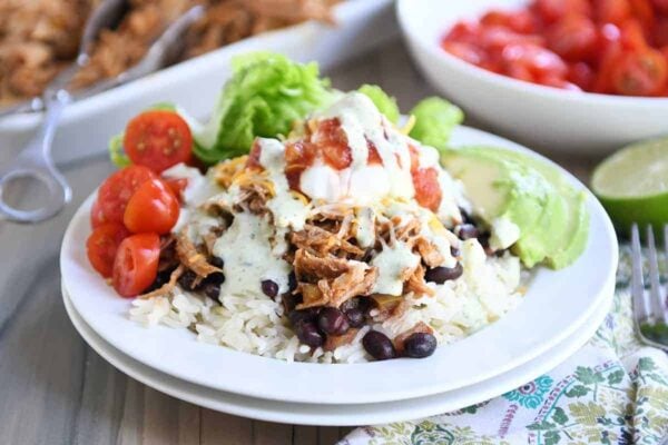 White plate with cilantro lime rice, black beans, sweet pork and toppings.