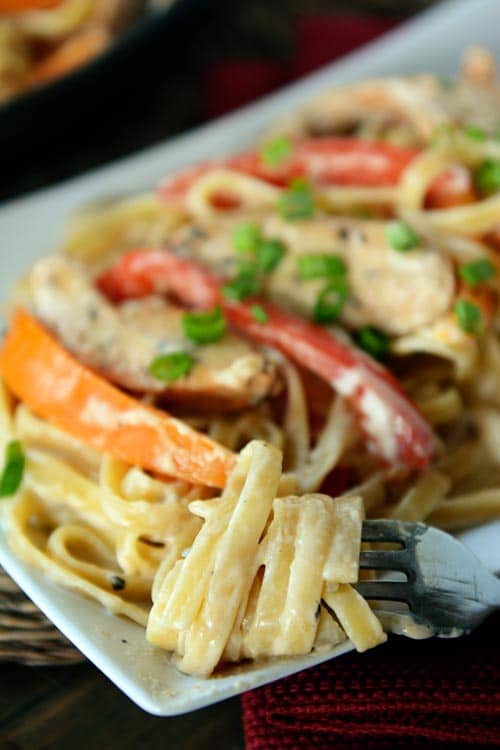 A fork with creamy fettucine wrapped around it from a platter of chicken cajun pasta. 