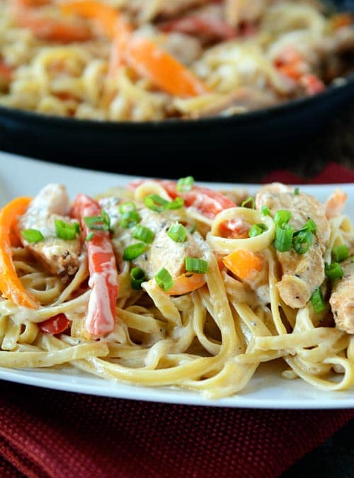 Cajun chicken pasta on a white platter with a skillet of pasta behind it. 