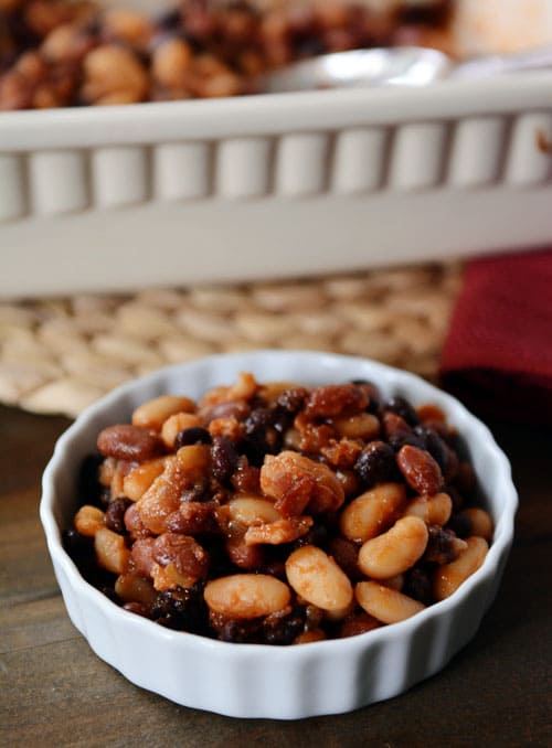 A small white ramekin filled with bacon-filled baked beans. 