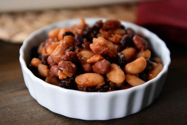 A white ramekin filled with bacon and baked beans. 