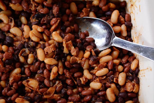 Big metal spoon stirring a large dish of baked beans. 