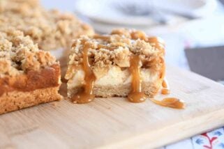 Caramel apple cheesecake bar drizzled with caramel on wood cutting board.