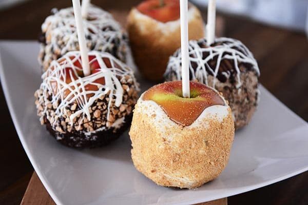 Five dipped and decorated caramel apples on a white platter.