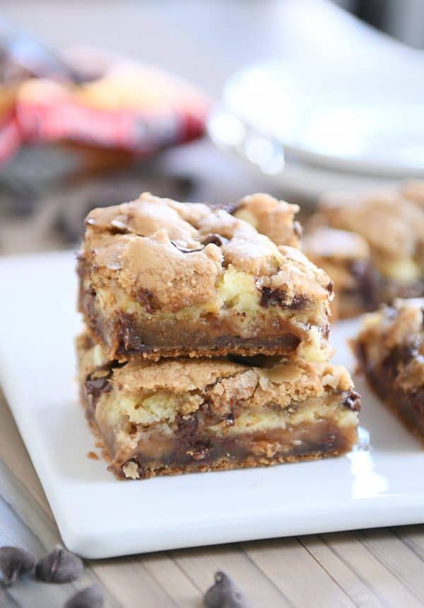 Two caramel cheesecake stuffed chocolate chip cookie bars stacked on white tray.