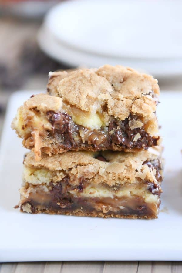 Two caramel cheesecake stuffed chocolate chip cookie bars stacked with bite taken out of top bar.