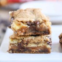 Two caramel cheesecake stuffed chocolate chip cookie bars stacked.
