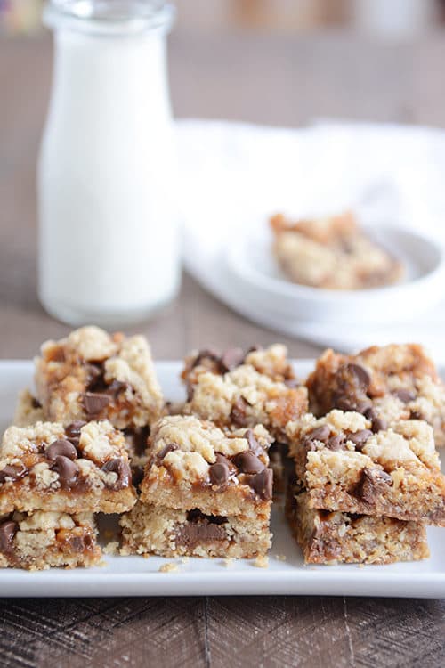 Caramel chocolate chip cookie bars on a white platter in front of a glass jar of milk.