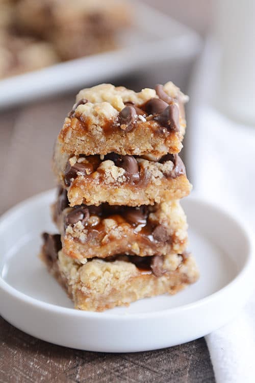 Four stacked up caramel chocolate chip cookie bars on a small round plate.