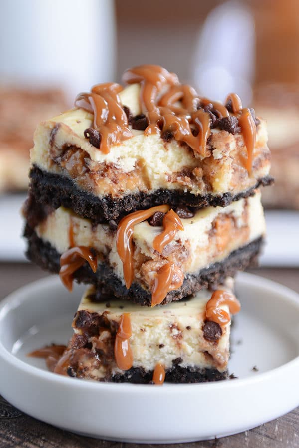 Caramel Snickers cheesecake bars stacked on top of each other in a white ramekin.
