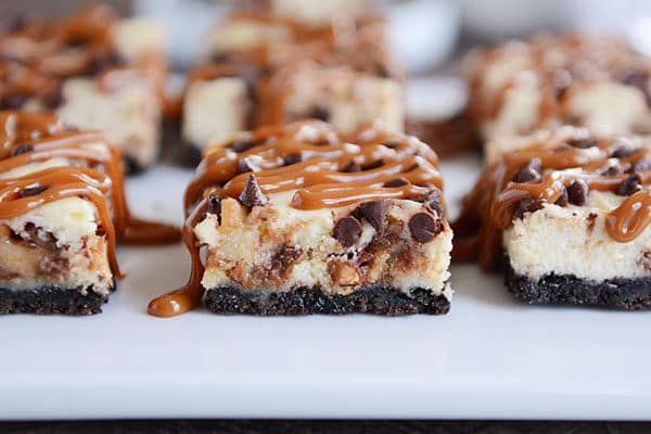 Caramel drizzled cheesecake cookie bars on a white countertop. 