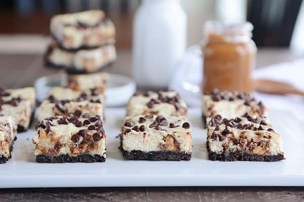 Chocolate chip sprinkled cheesecake bars with an Oreo crust on a white platter.
