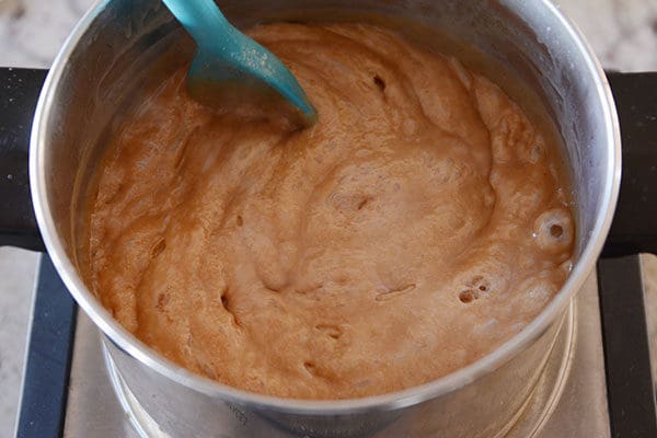 A pot of bubbling caramel getting stirred by a plastic spoon.