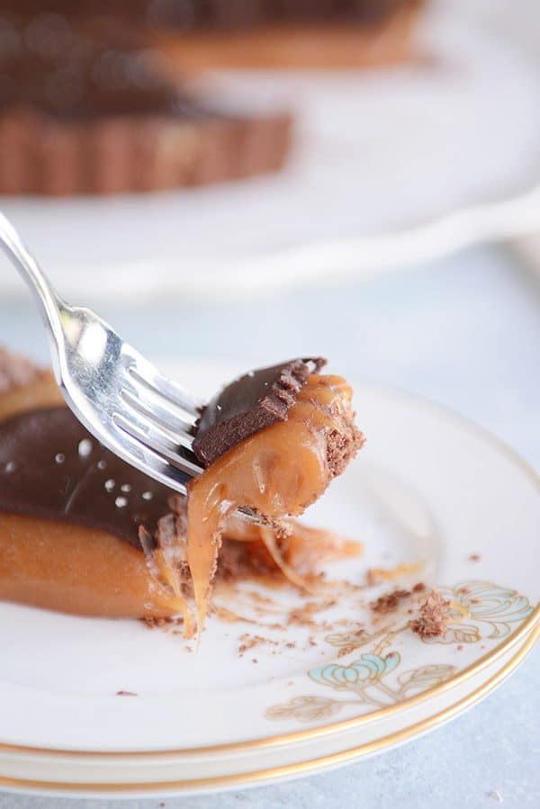 A fork taking a bite out of a slice of decadent caramel chocolate tart. 