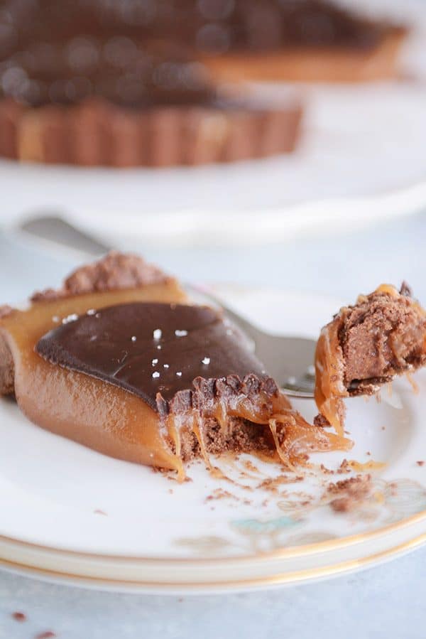 A slice of caramel chocolate tart with a fork taking a bite out. 
