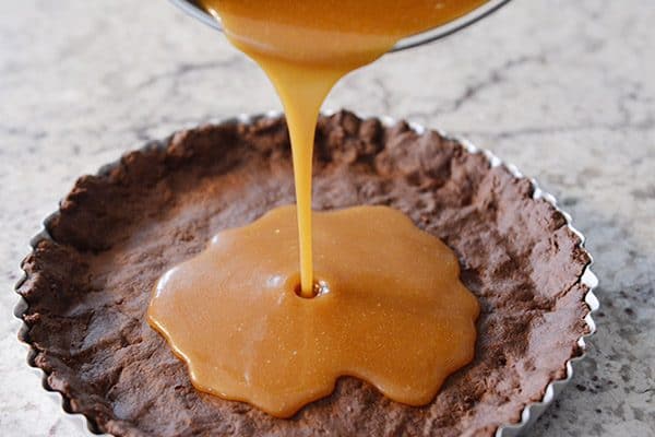 Caramel getting poured into a chocolate tart crust. 