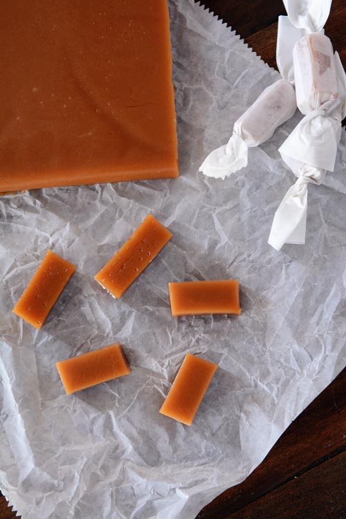 Pieces or caramel, some wrapped and some not, sitting next to a big slab of caramel.