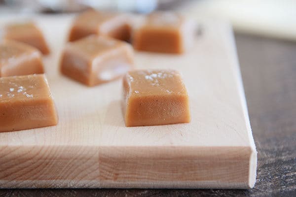 Squares of vanilla bean caramel cut up on a wooden cutting board.