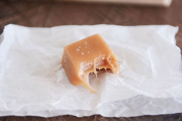 A square of salted vanilla bean caramel with a bite taken out on a piece of parchment.
