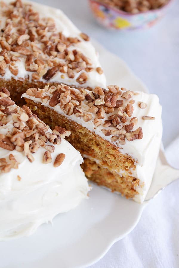 A plate of cake topped with chopped nuts, and one slice cut and being pulled out. 