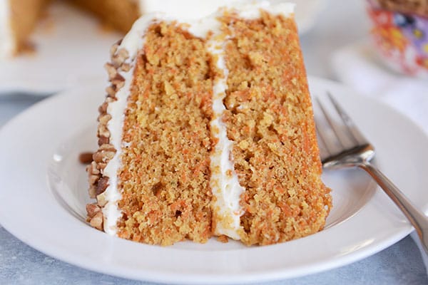 A slice of carrot cake with two layers, white frosting in the middle, and chopped nuts on top on a plate.