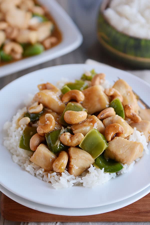 A large serving of white rice topped with saucy cashew chinese chicken with green peppers.
