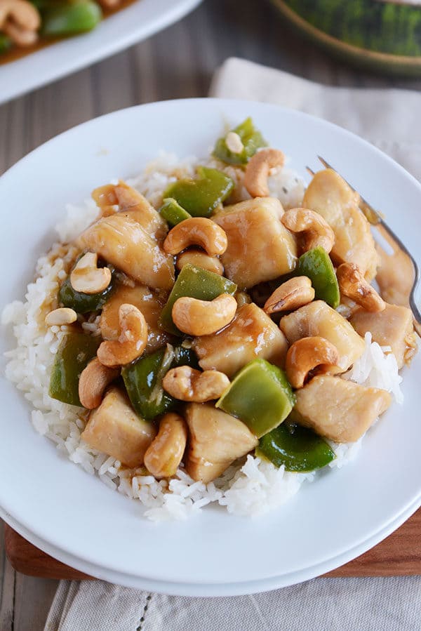 Top view of a white plate of cooked rice topped with cashew chinese chicken.
