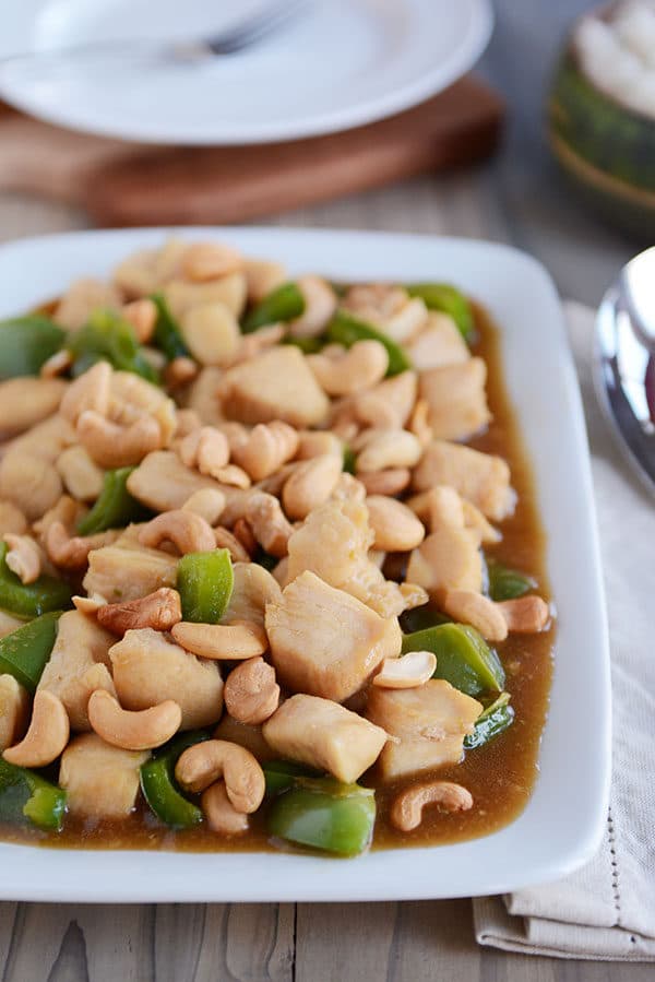 A white platter of saucy cashew chicken with large green pepper chunks mixed in.