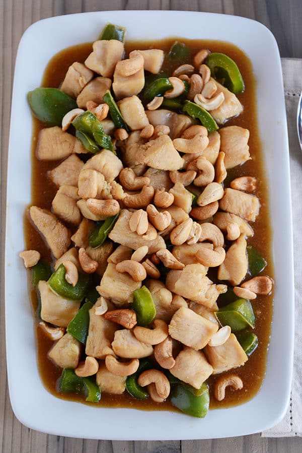 Top down view of a large white platter of chinese cashew chicken with sauce and green peppers.