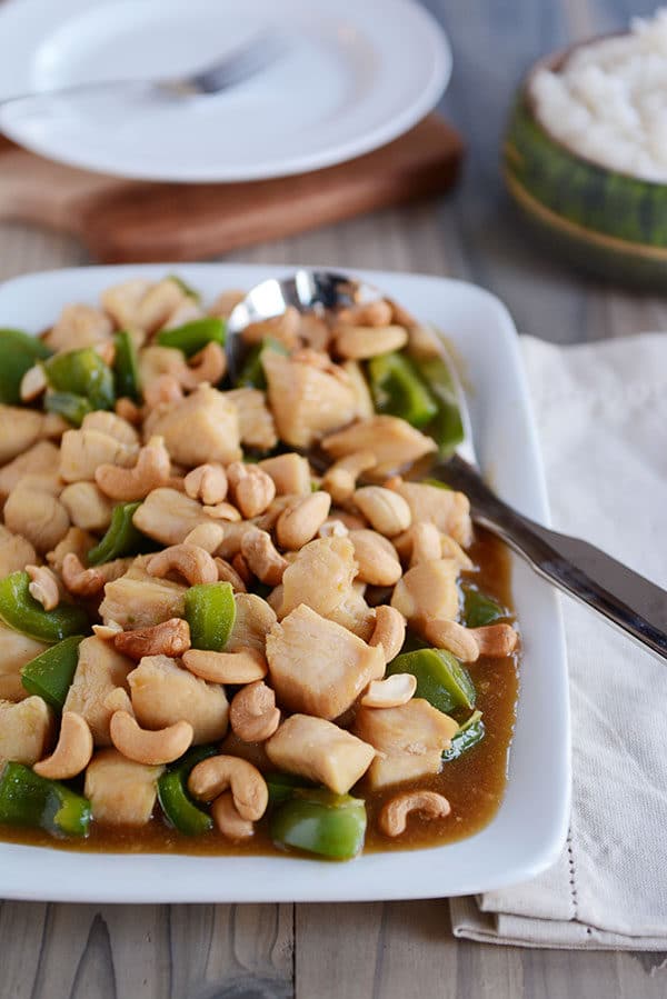 A large metal spoon on a white tray of saucy chinese cashew chicken.