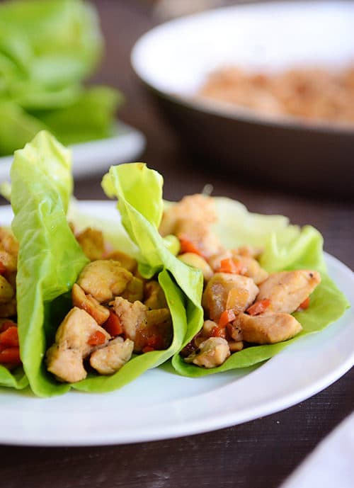 A white plate with three cashew chicken lettuce wraps.