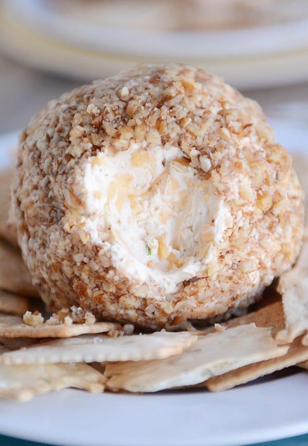 Large cheeseball with pecan crusted outside on a plate with crackers around it.