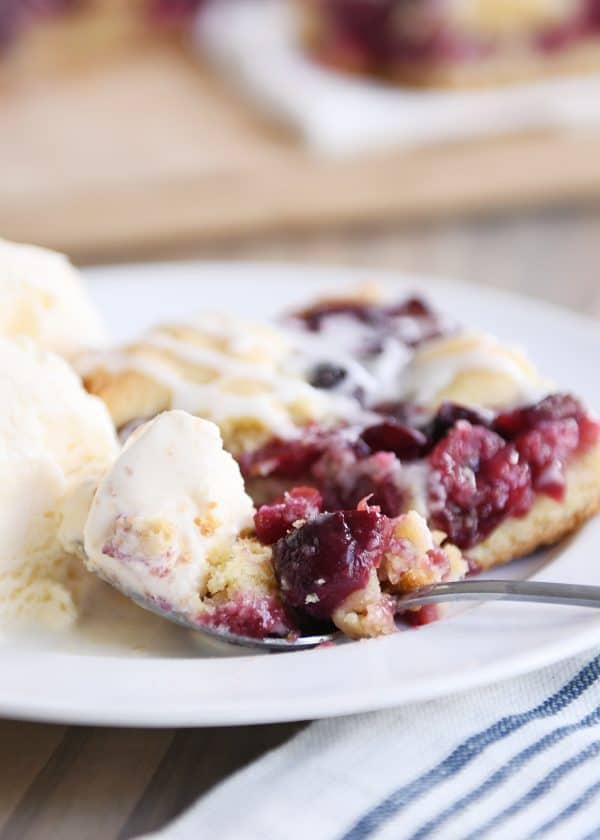 Cherry pie cookie bar on white plate with scoop of ice cream.