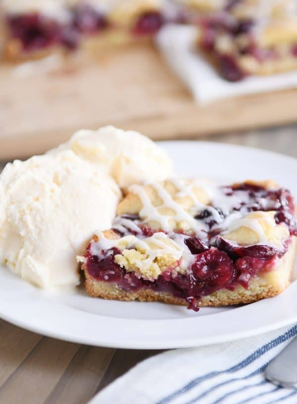 A large piece of cherry pie cookie bar next to a scoop of vanilla ice cream.