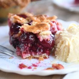 Bite taken out of cherry pie with scoop of vanilla ice cream next to it.