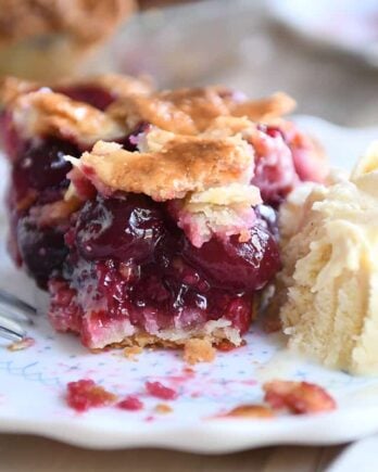 Bite taken out of cherry pie with scoop of vanilla ice cream next to it.