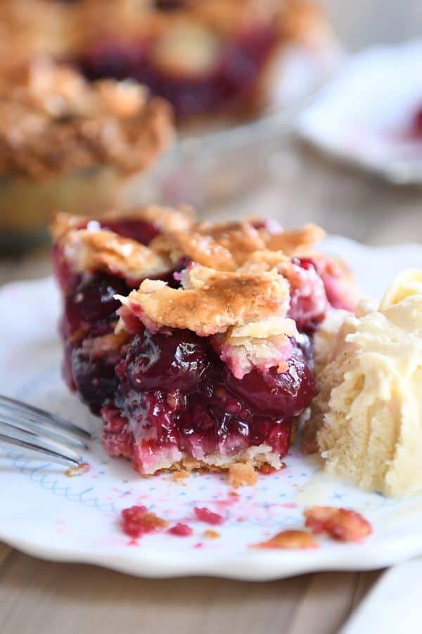 Bite taken out of cherry pie with scoop of vanilla ice cream next to it.