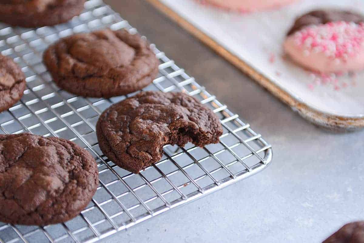 Chocolate cookies on a cooling rack, one with a bite taken out.