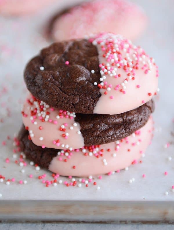 A stack of chocolate cookies half dipped in frosting and sprinkles.