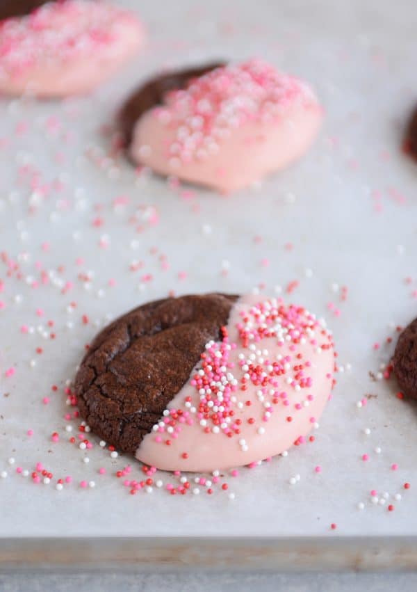Chocolate cookies half-dipped in frosting and sprinkles.