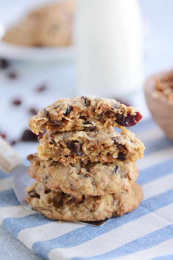 A stack of chewy granola cookies on a blue and white napkin with the top cookie split in half.