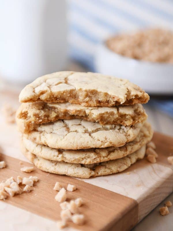 Stack of toffee cookies on wood cutting board with one cookie broken in half.